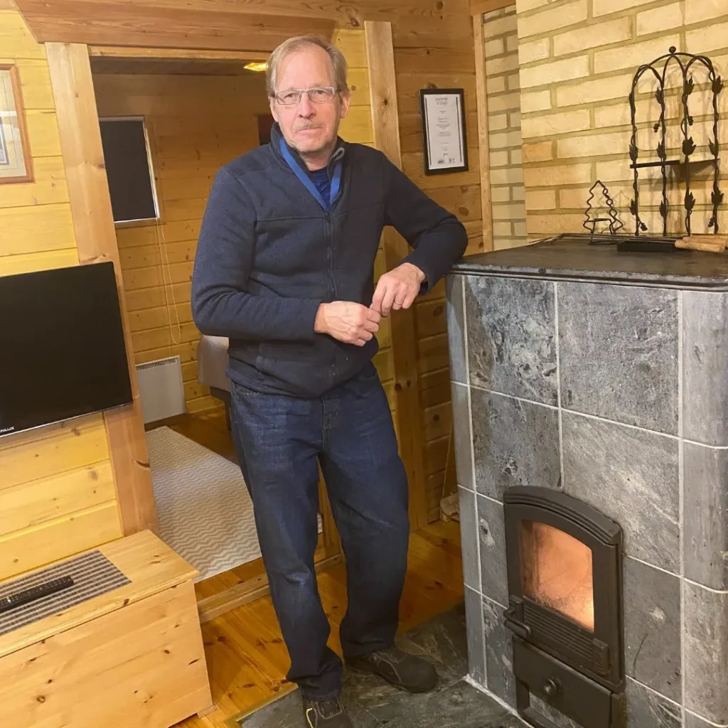 Yrittäjä Hannu nojaa takkaan Pärnävaaran huvilassa Liperissä Pohjois-Karjalassa – viihtyisää majoitusta vaaramaisemassa.