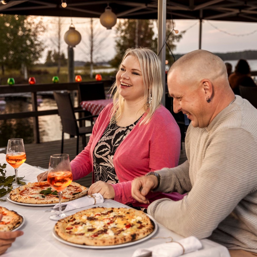 Pariskunta nauttii pizzaa Saariston Puodin pihassa Liperin satamassa Pohjoisella Saimaalla, sataman yhteydessä on myös paikkoja asuntoautoille.