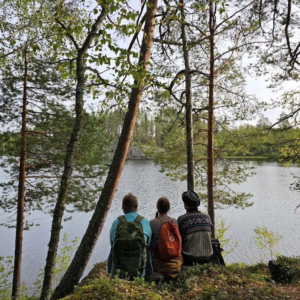 Ihmiset istuvat rannalla puiden alla – Metsäakkunan luonto-opastukset Valamon tukikohdasta.