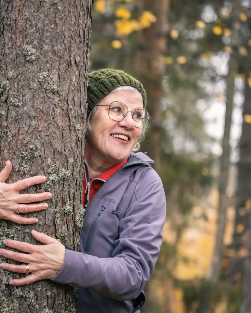 Nainen nojaa puuhun metsässä Liperissä Pohjoisella Saimaalla – luonnossa liikkuminen ja rauhoittuminen ovat osa alueen aktiviteetteja.