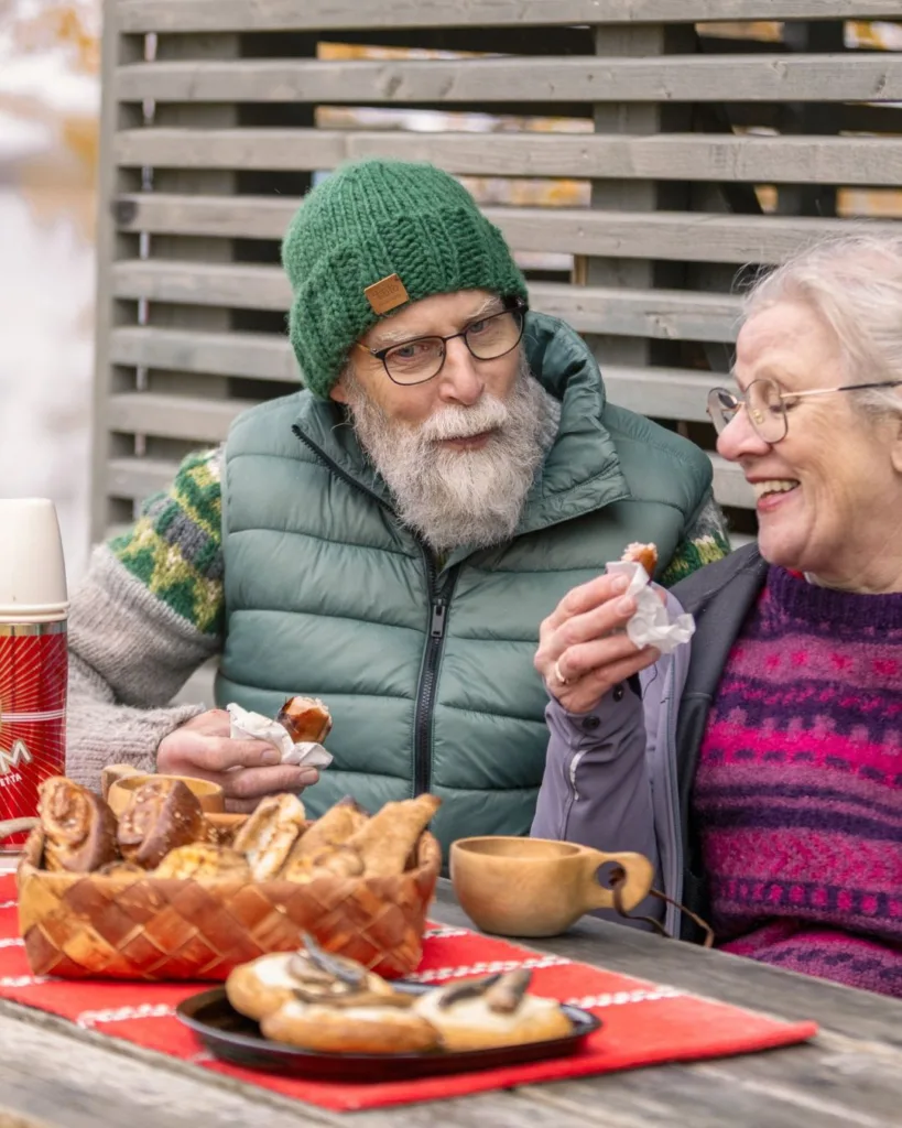 Senioripari nauttii eväitä Pohjoisella Saimaalla hirsipöydältä. jolla karjalanpiirakoita, pyöröjä ja savumuikkua.