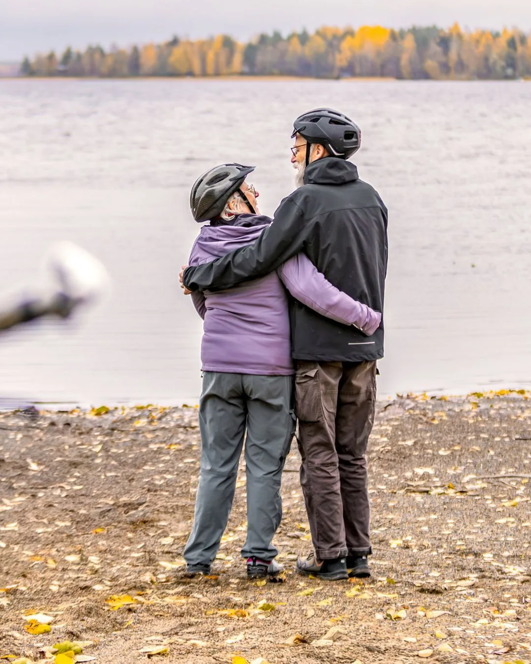 Senioripari katsoo toisiinsa hiekkarannalla pyöräilykypärät päässä – useat pyöräilyreitit kulkevat satamien kautta.