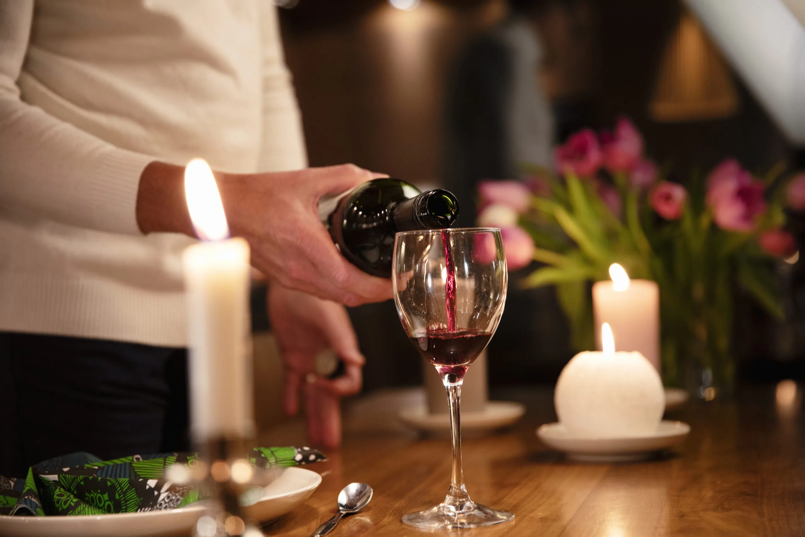 A man's hand pours red wine into a glass in atmospheric lighting in North Karelia - check out the catering services and meeting facilities on the home page.