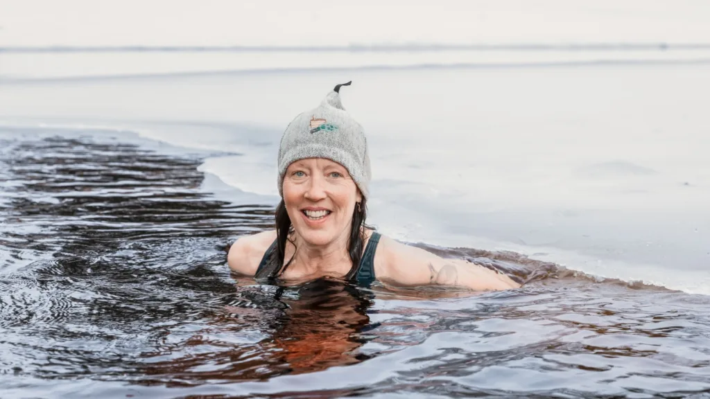 Nainen hymyilee avannossa Pohjois-Karjalassa – vastuullisia talvielämyksiä Pohjoisella Saimaalla lähellä Koli ja Joensuu.