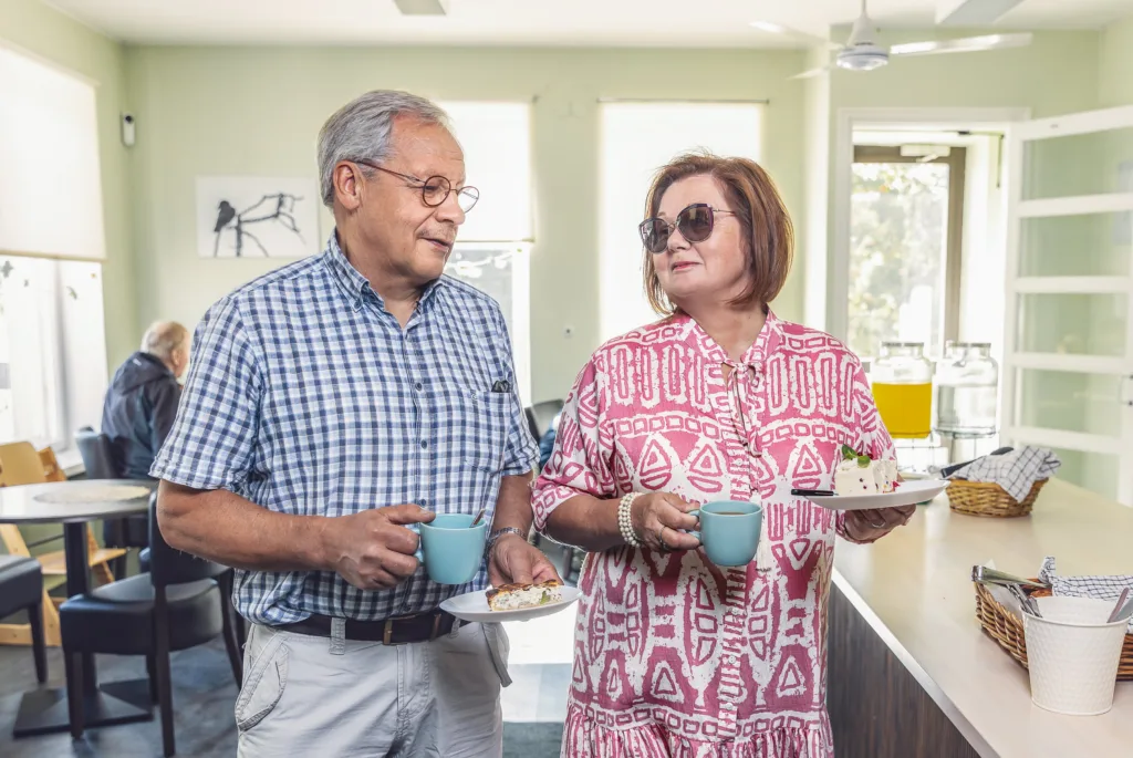 Pariskunta hymyilee kakkulautaset käsissään kahvilassa Pohjois-Karjalassa – nauttien paikallisista herkuista iloisessa tunnelmassa.