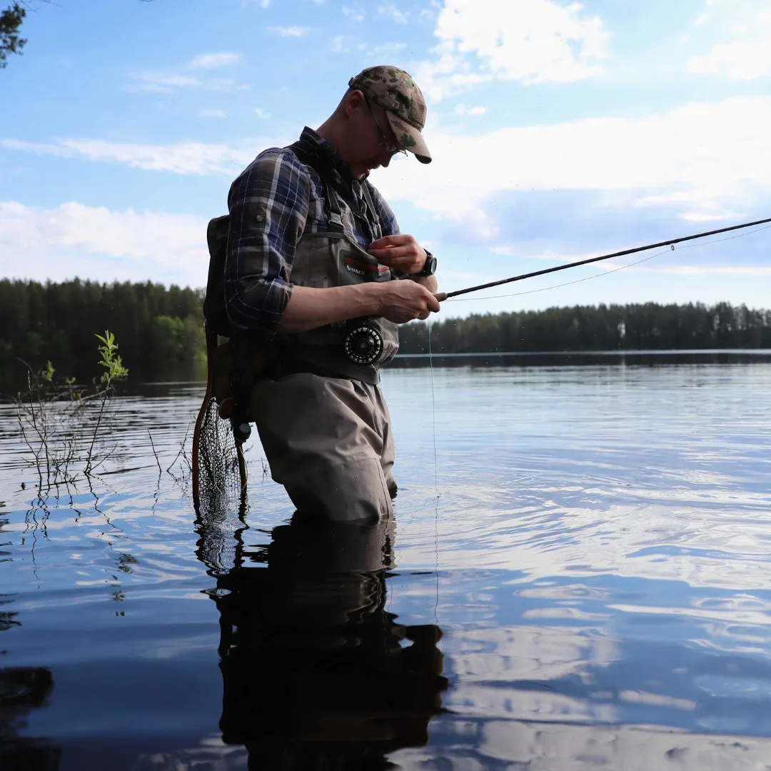 Kalastaja seisoo järvessä Pohjois-Karjalassa – koe opastetut kalastus- ja melontaelämykset aktiviteeteissa.