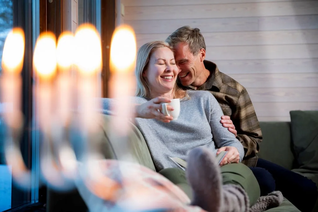 Pariskunta rentoutuu sohvalla kodikkaassa majoituksessa Pohjoisen Saimaan alueella Pohjois-Karjalassa – rauhallinen ja mukava lomakoti.