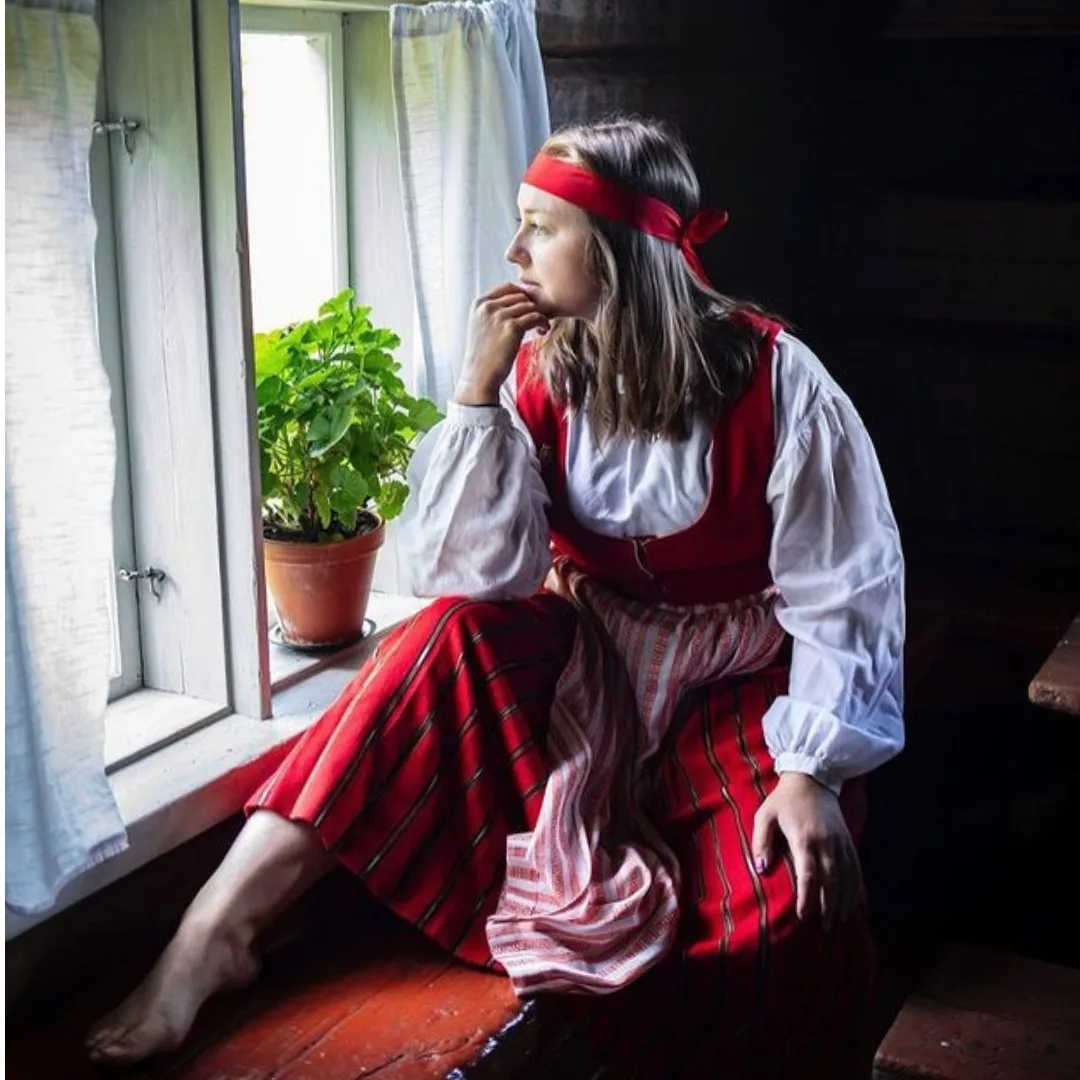 Nuori nainen kansallispuvussa katsoo ikkunasta – talkootyöllä syntyviä tapahtumia, käyntikohteita ja nähtävyyksiä vastuullisesti.