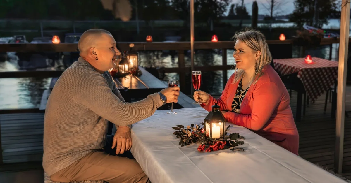 Nuoripari hymyilee leveästi viinilasit käsissä tunnelmallisessa ravintolassa.