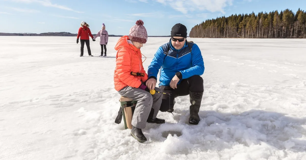 Familie Eisangeln, Mann bohrt ein Loch ins Eis mit Kind in Nordkarelien – verantwortungsvolle Familienaktivitäten ohne Angelschein.