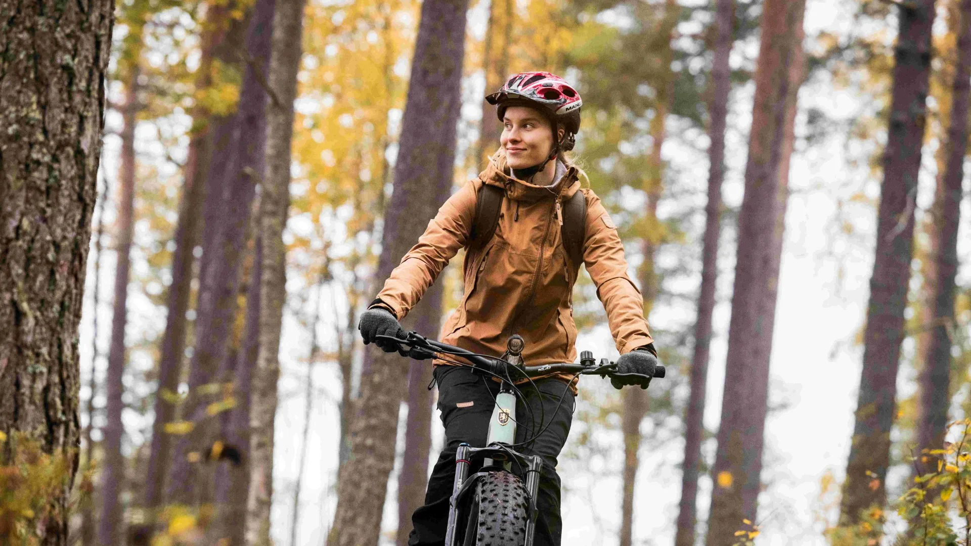 Nuori nainen pyöräilee maastopyörällä syksyisessä metsässä Pohjois-Karjalassa – tutustu pyöräilyreitteihin Pyöräilyreitit-sivulta.